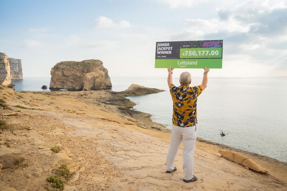 Lottoland winner holding up cheque facing the sea